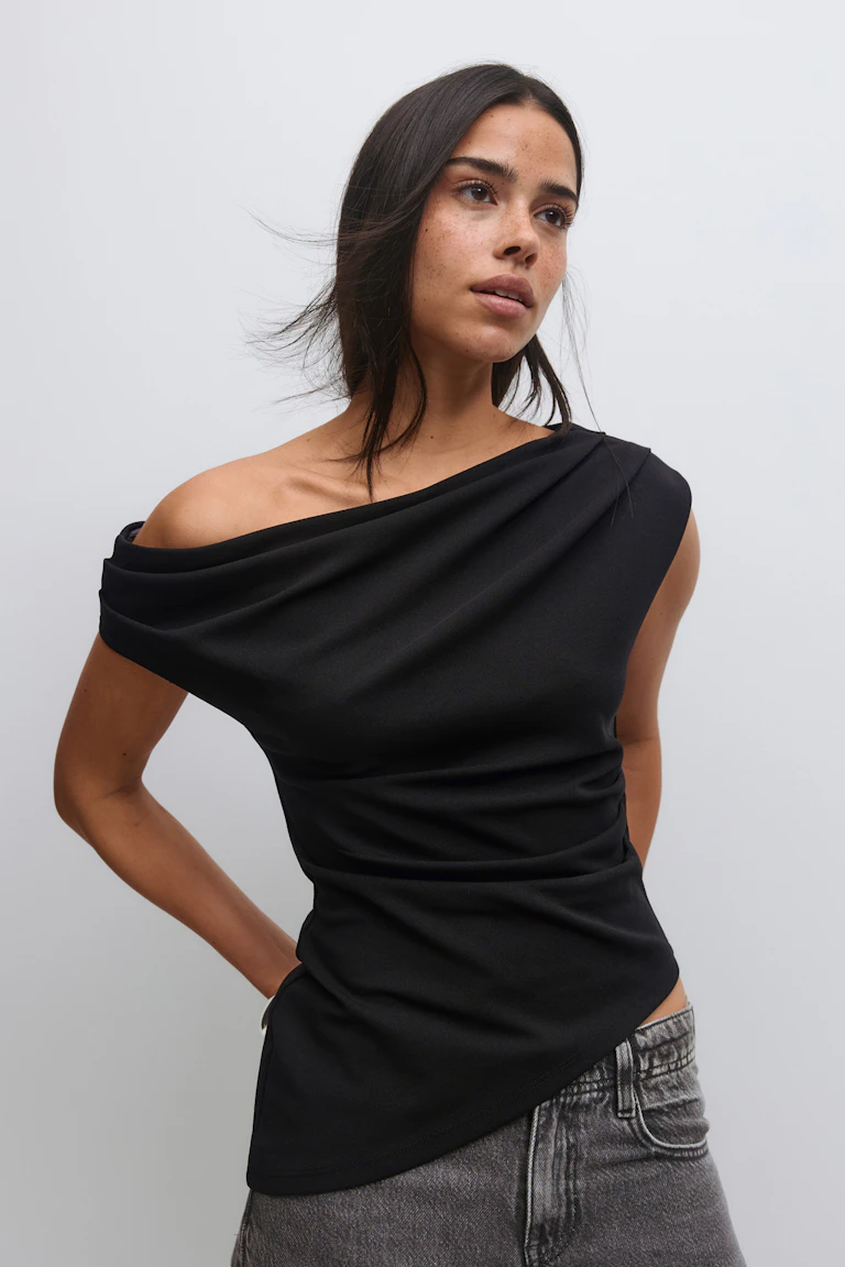 Schwarzes, asymmetrisches, schulterfreies, drapiertes Oberteil mit kurzen Ärmeln, gepaart mit hochtaillierten, verwaschenen grauen Jeans.