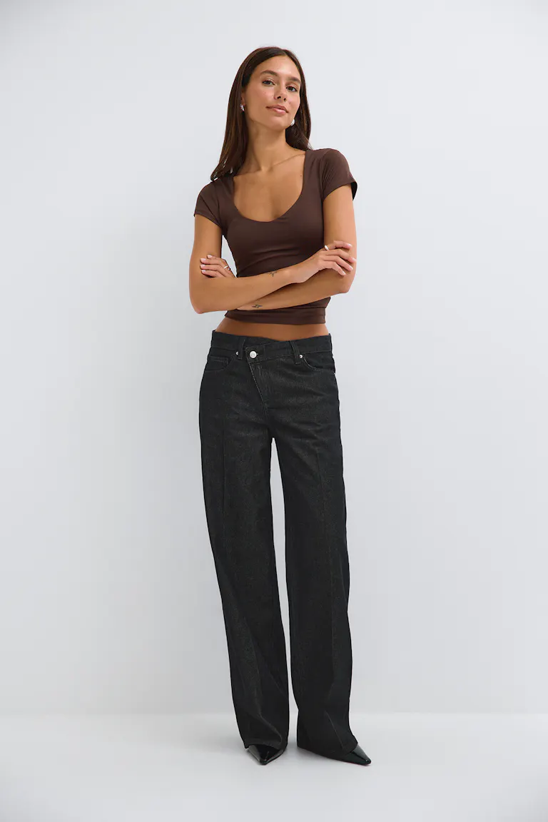 She wears a fitted brown short-sleeve scoop-neck top, black wide-leg jeans, and black pointed-toe heels.