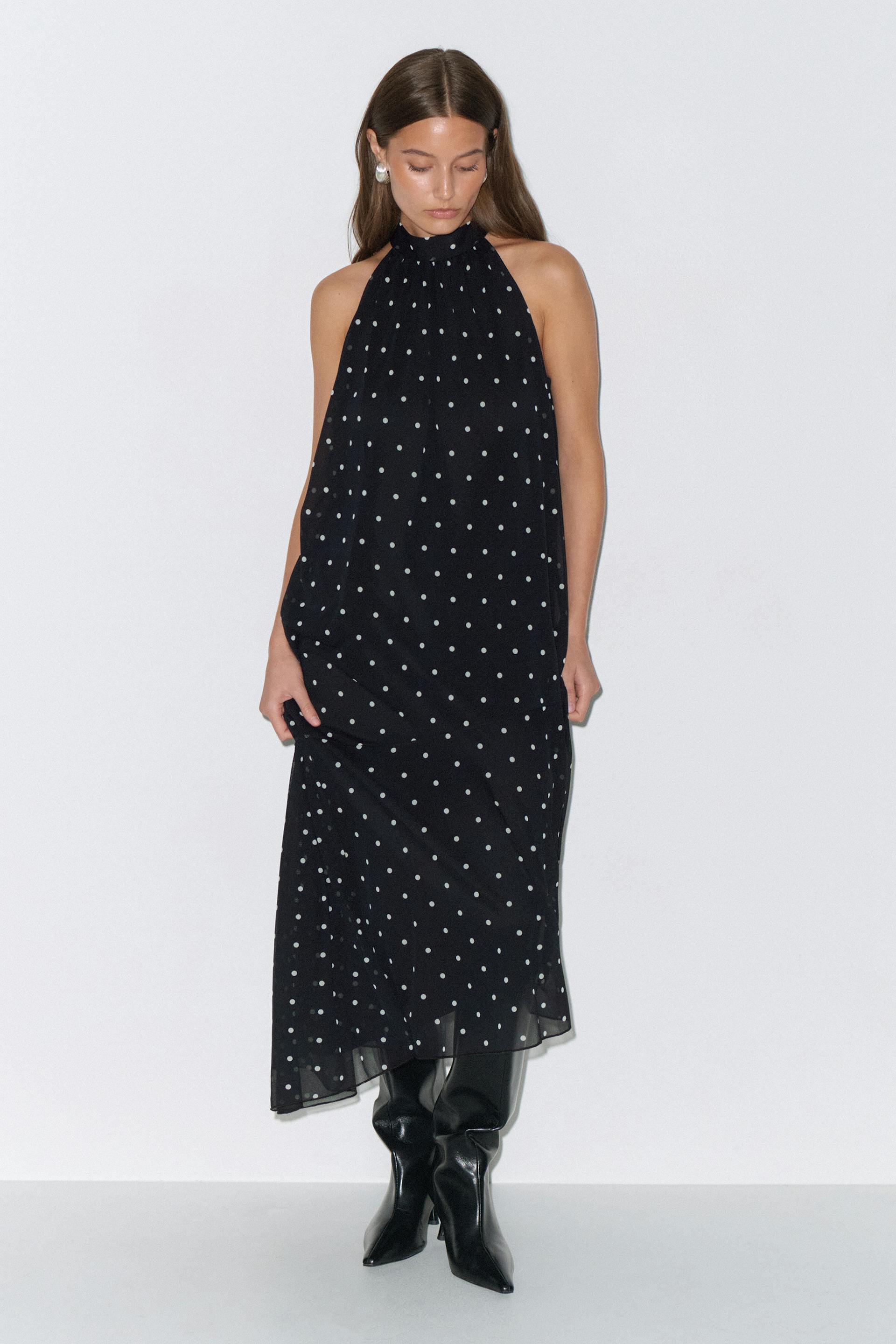Black sleeveless halter-neck midi dress with white polka dots, styled with glossy black knee-high pointed-toe boots and pearl stud earrings.