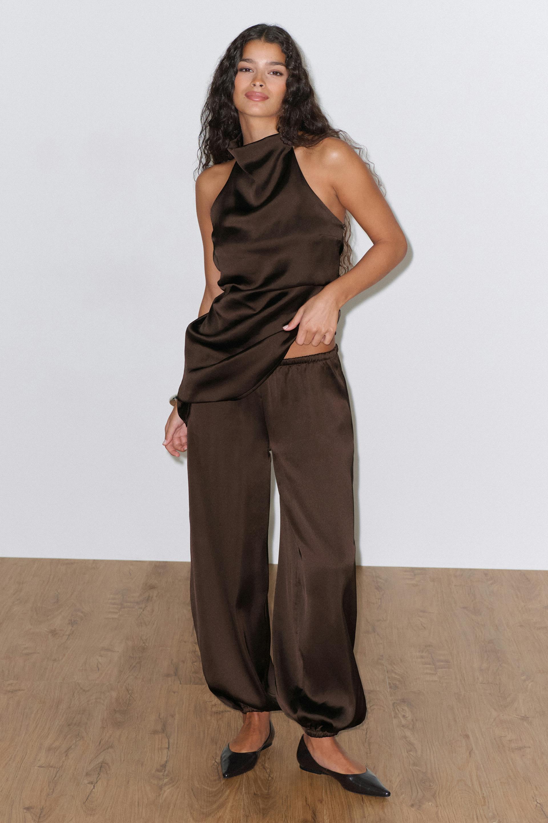 Chocolate-brown satin halter-neck sleeveless top paired with matching wide-leg elastic-cuff trousers and black pointed-toe flats.
