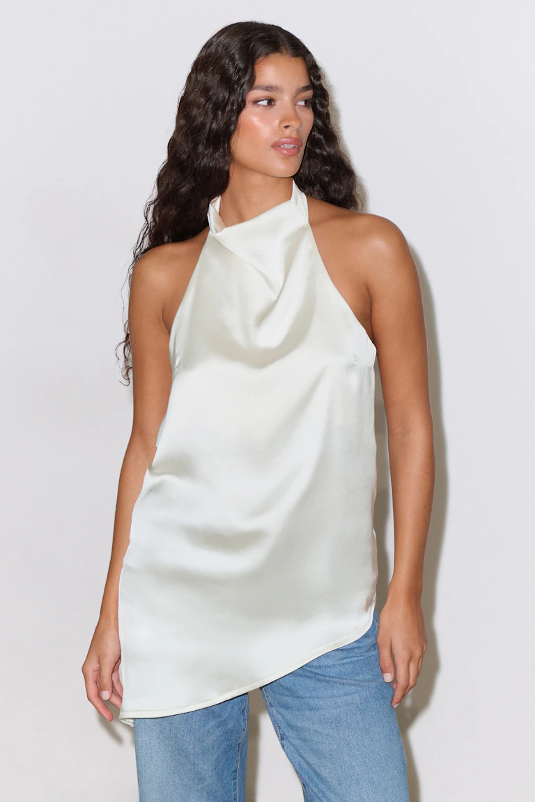 Elfenbeinfarbenes Satin-Trägertop mit drapiertem Kuttenausschnitt und asymmetrischem Saum, kombiniert mit hellblauen Denim-Jeans.