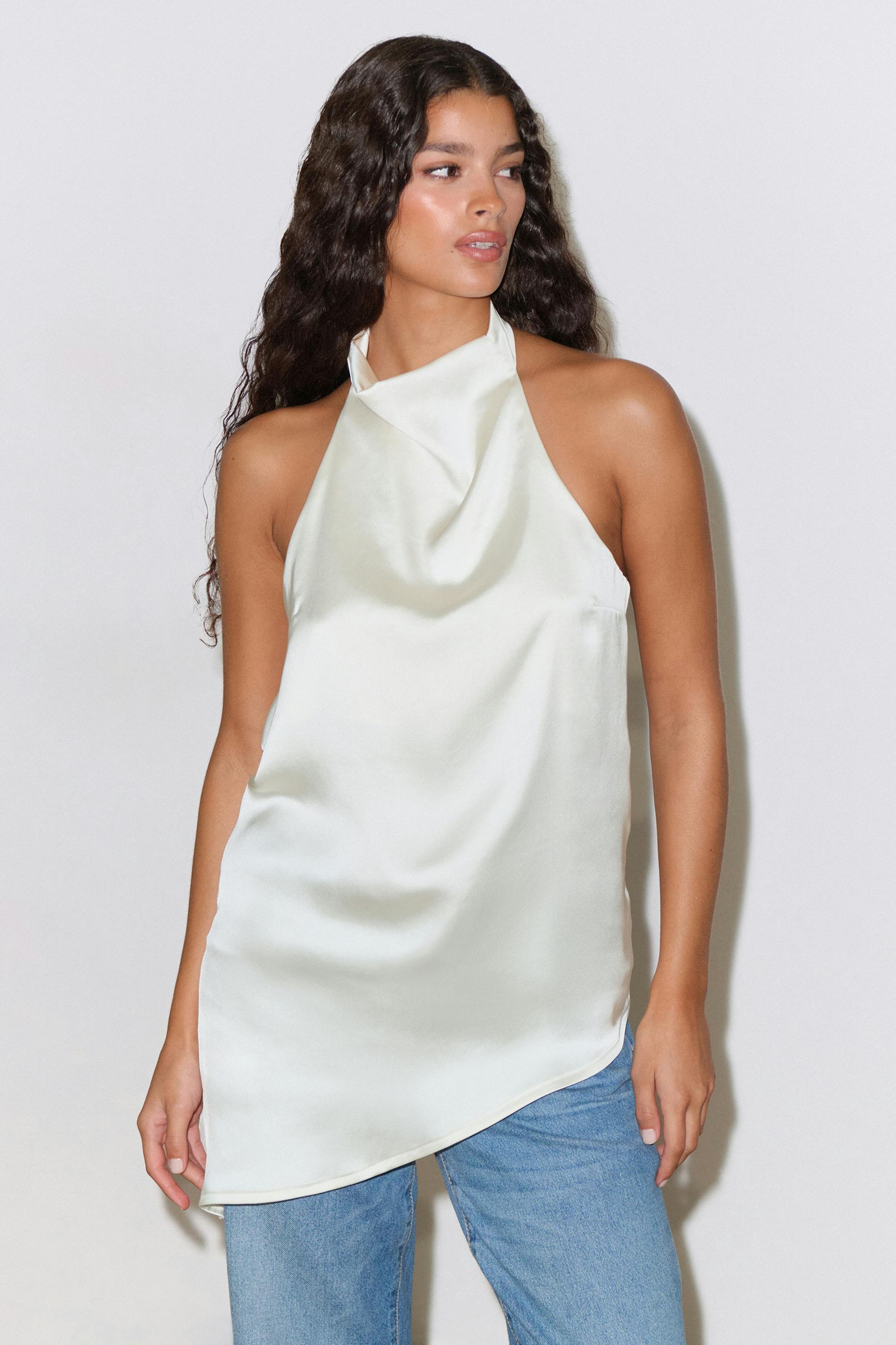 Top licou en satin ivoire avec encolure drapée et ourlet asymétrique, associé à un jean bleu clair.