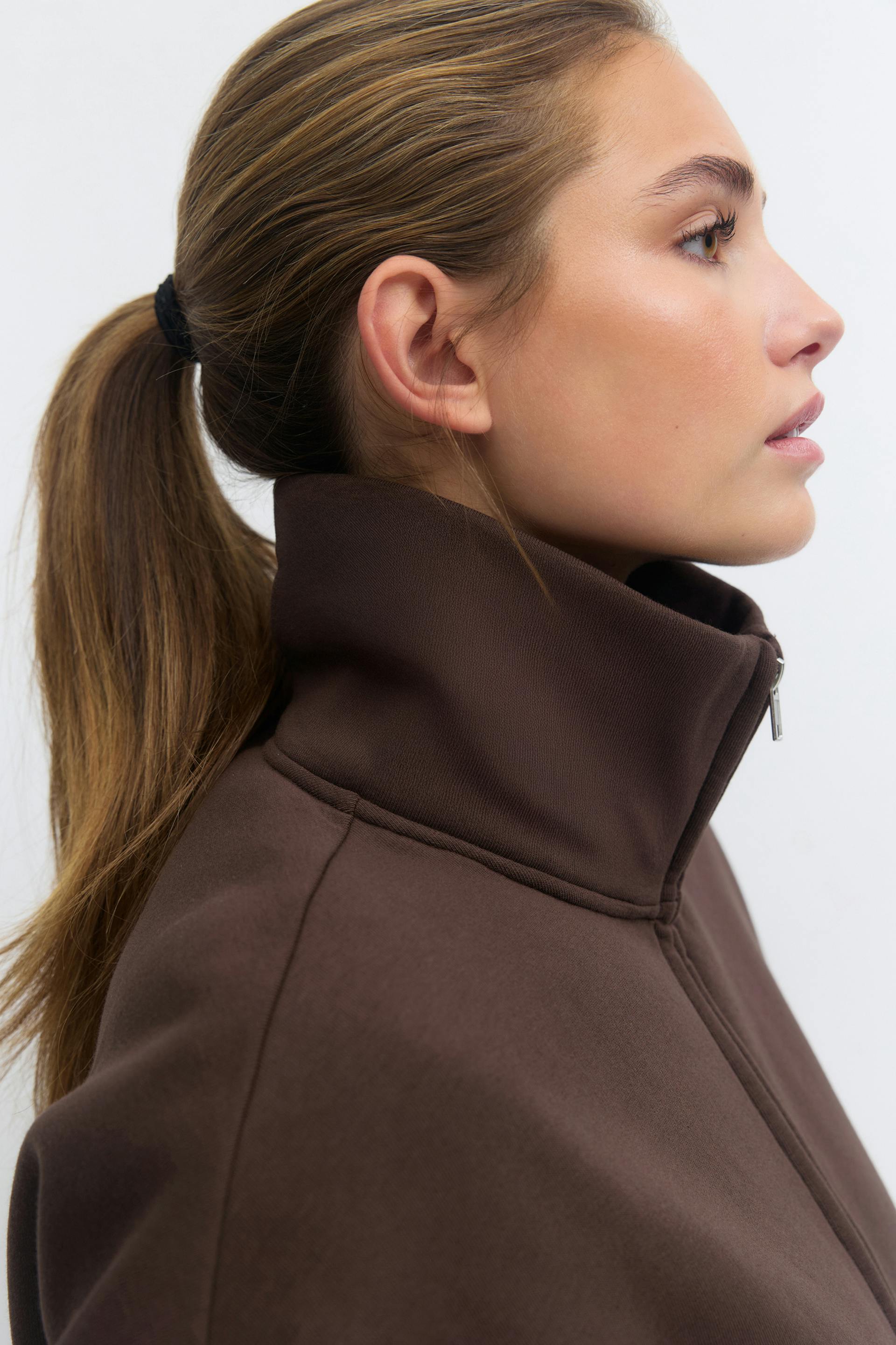 Tummanruskea vetoketjullinen collegepaita, jossa on korkea kaulus.