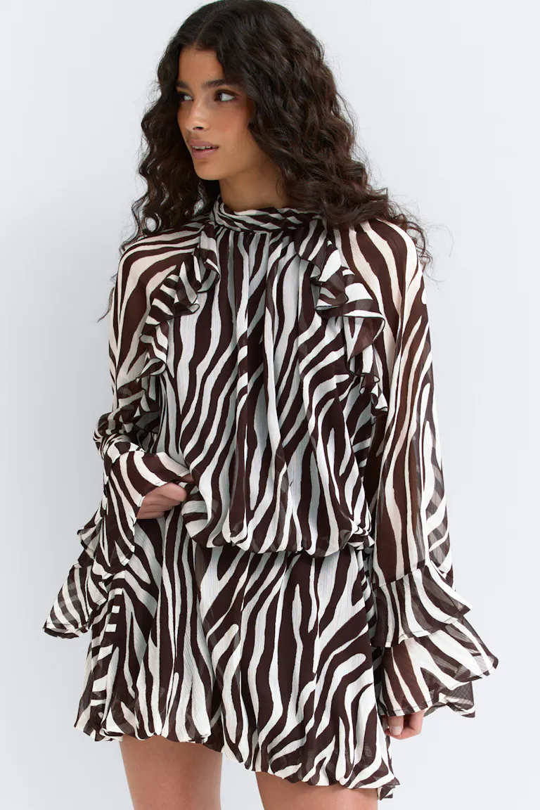 Brun-hvid zebraprintet chiffon-minikjole med lange ærmer, høj flæseudskæring, blouson i taljen og flæsedetaljer på skuldre, manchetter og forneden.