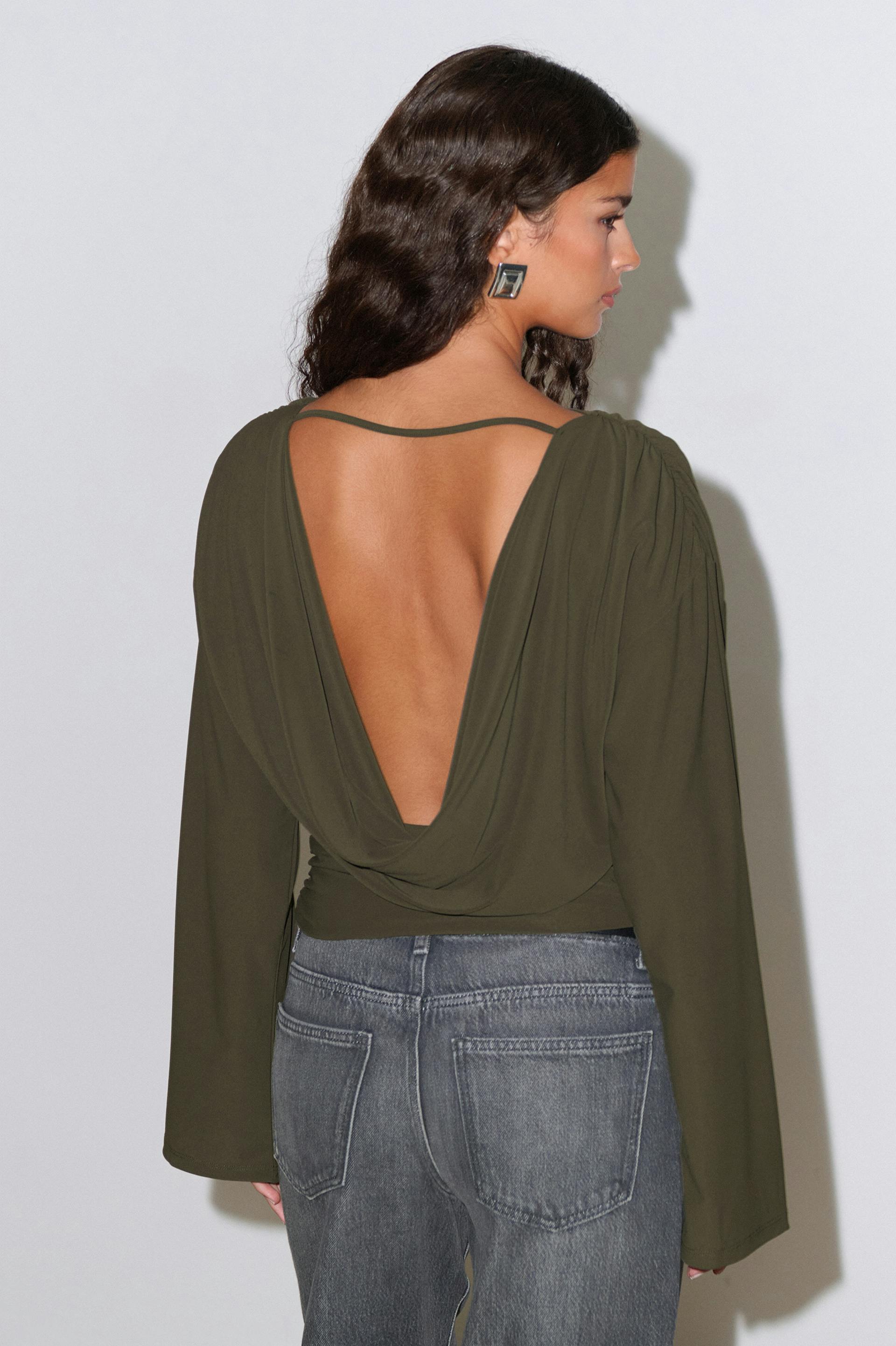 Olivgrünes, langärmeliges, drapiertes Oberteil mit tiefem, offenem Rücken und dünnen Schulterträgern, kombiniert mit verwaschenen grauen High-Waist-Jeans.