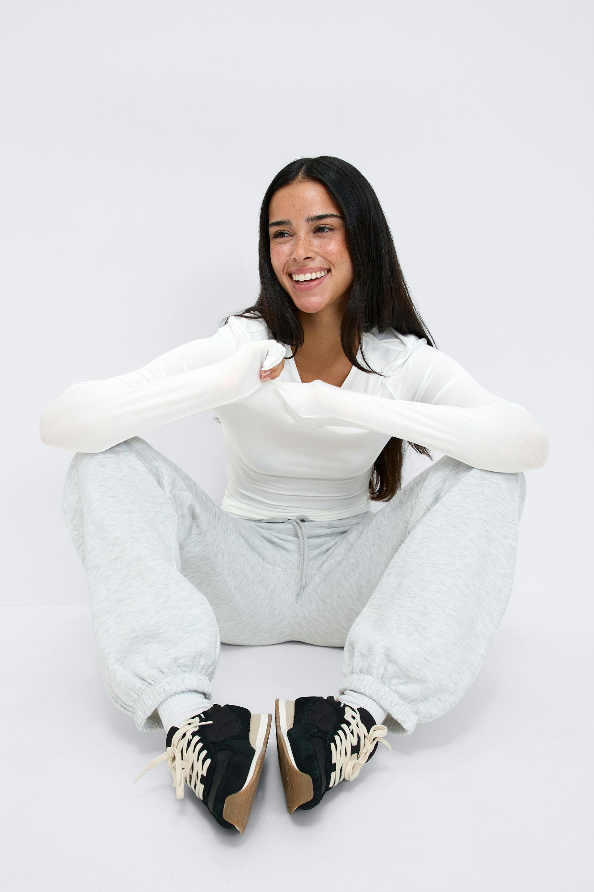 Hvit langermet topp med forlengede ermer, lysegrå joggebukse med elastisk mansjett, hvite sokker og svarte joggesko med kremfargede lisser og gummisåler.