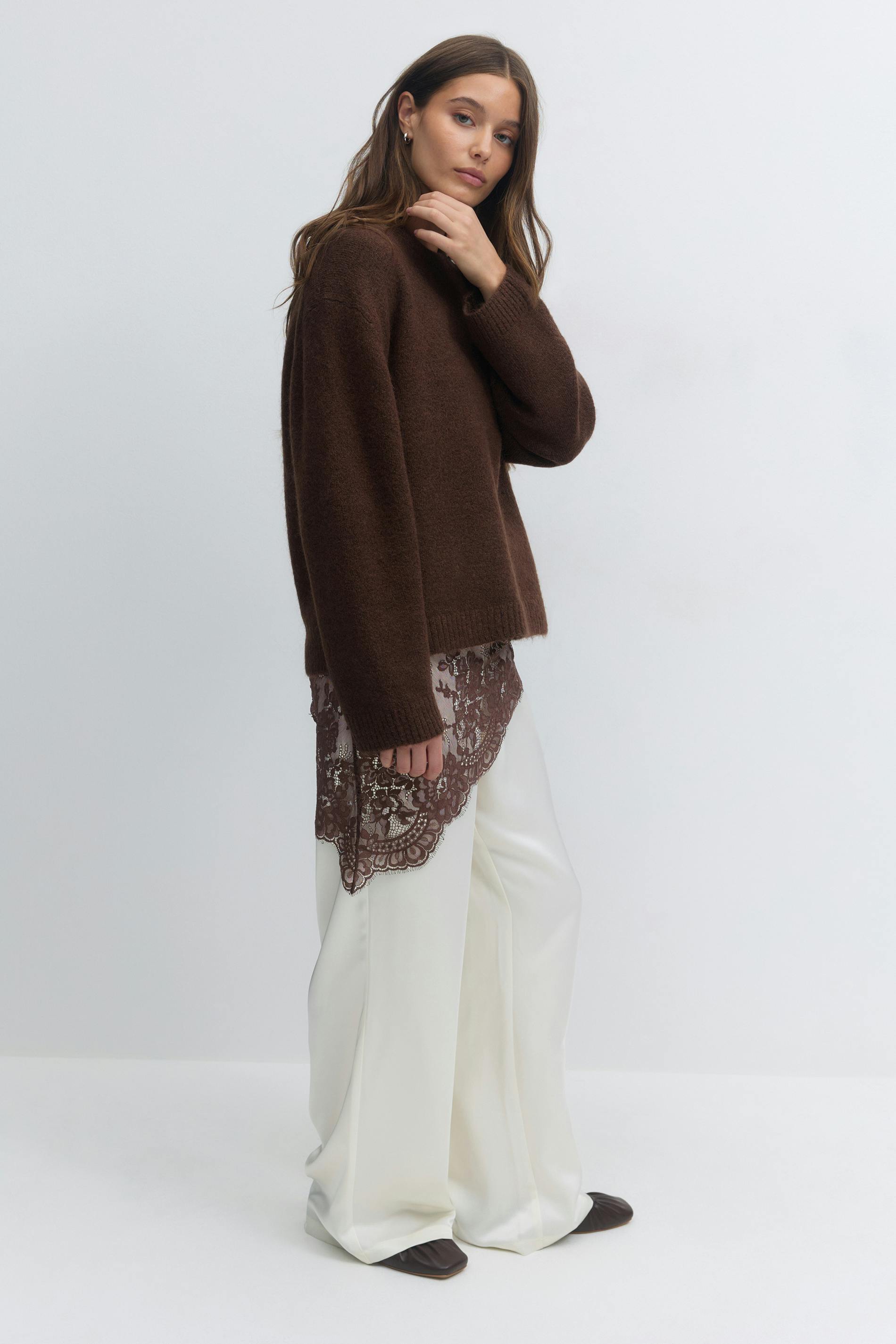 Brown oversized knit sweater layered over a brown lace-trim camisole, paired with white wide-leg trousers and dark brown square-toe flats.