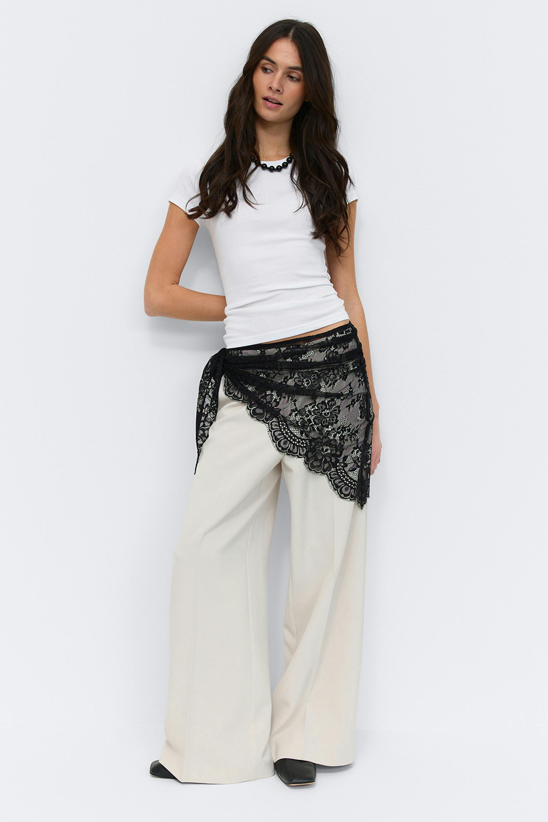 Tailored grey double-breasted wool jacket over a black turtleneck, paired with an asymmetrical black lace overlay, white wide-leg trousers and black pointed-toe heels.