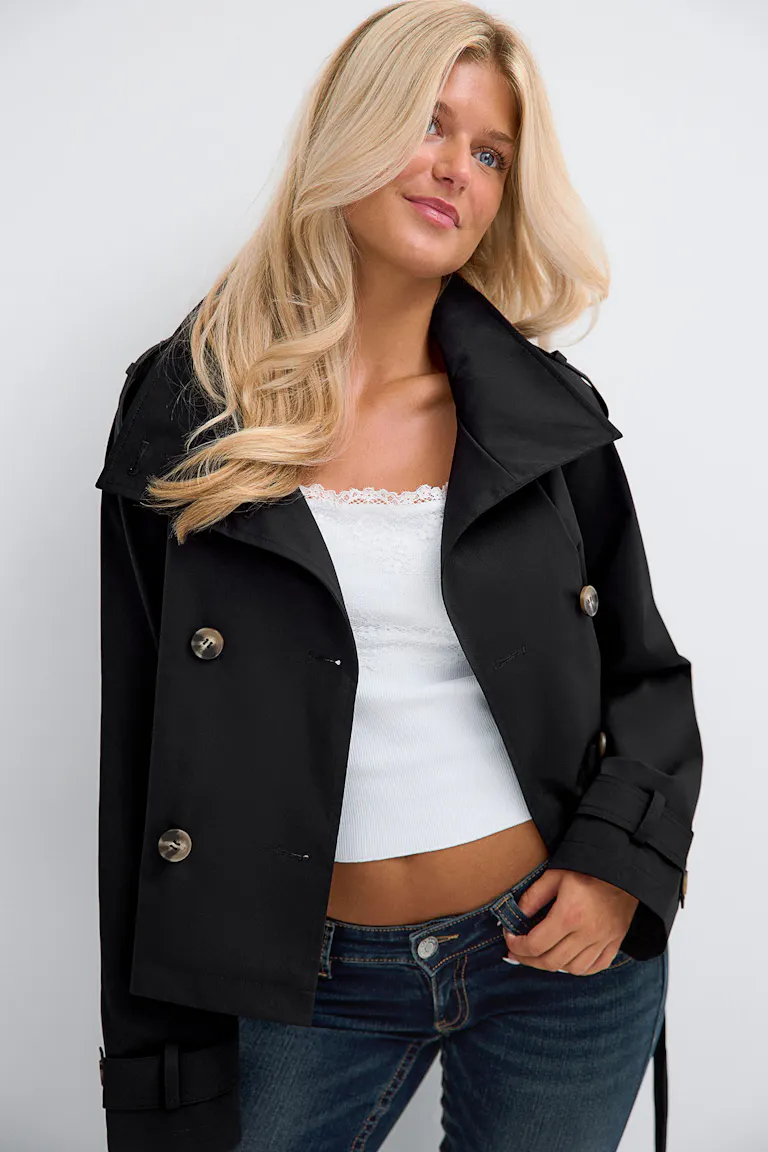 Black trench coat over a white lace-trimmed top with blue jeans.