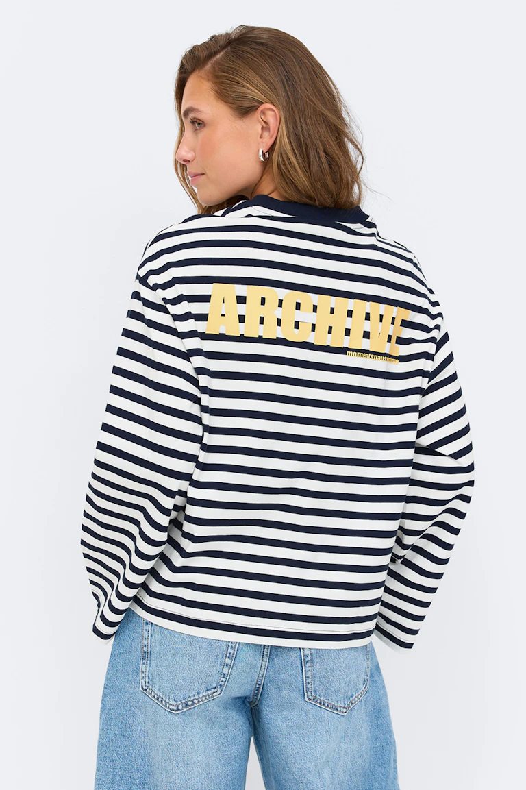Langermet topp med horisontale striper i marineblå og hvit med gult "ARCHIVE"-trykk på ryggen, kombinert med lyseblå denimjeans.
