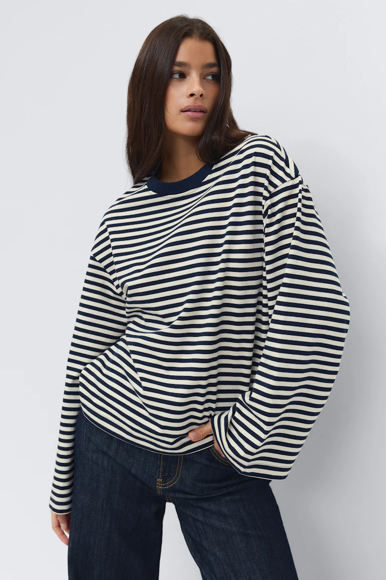 Långärmad oversized topp med horisontella ränder i marinblå och vit färg och marinblå rund halsringning, kombinerad med jeans i mörk indigo med kontrastsömmar.