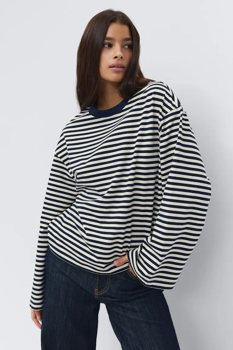 Marineblau-weißes, horizontal gestreiftes, langärmeliges Oversize-Top mit marineblauem Rundhalsausschnitt, kombiniert mit dunkelindigofarbenen Jeans mit Kontrastnähten.