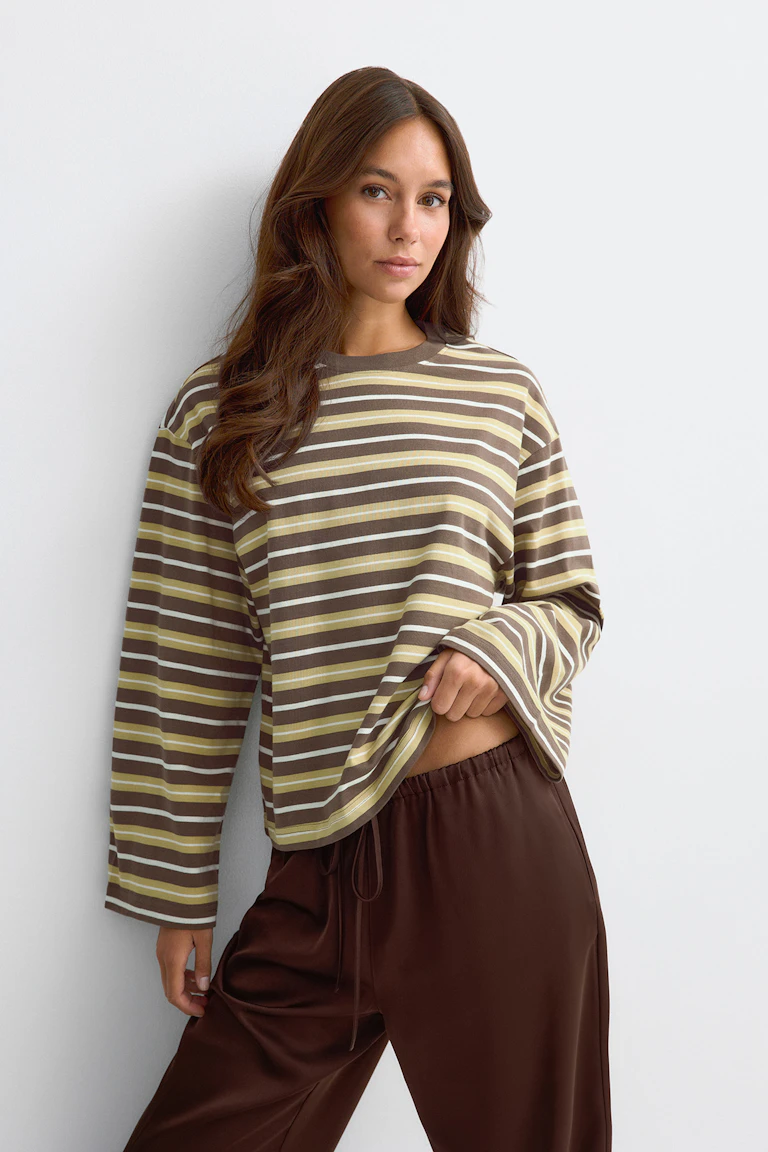 Modellen bär en randig långärmad tröja i brunt, beige och krämvitt, tillsammans med bruna byxor med dragsko.