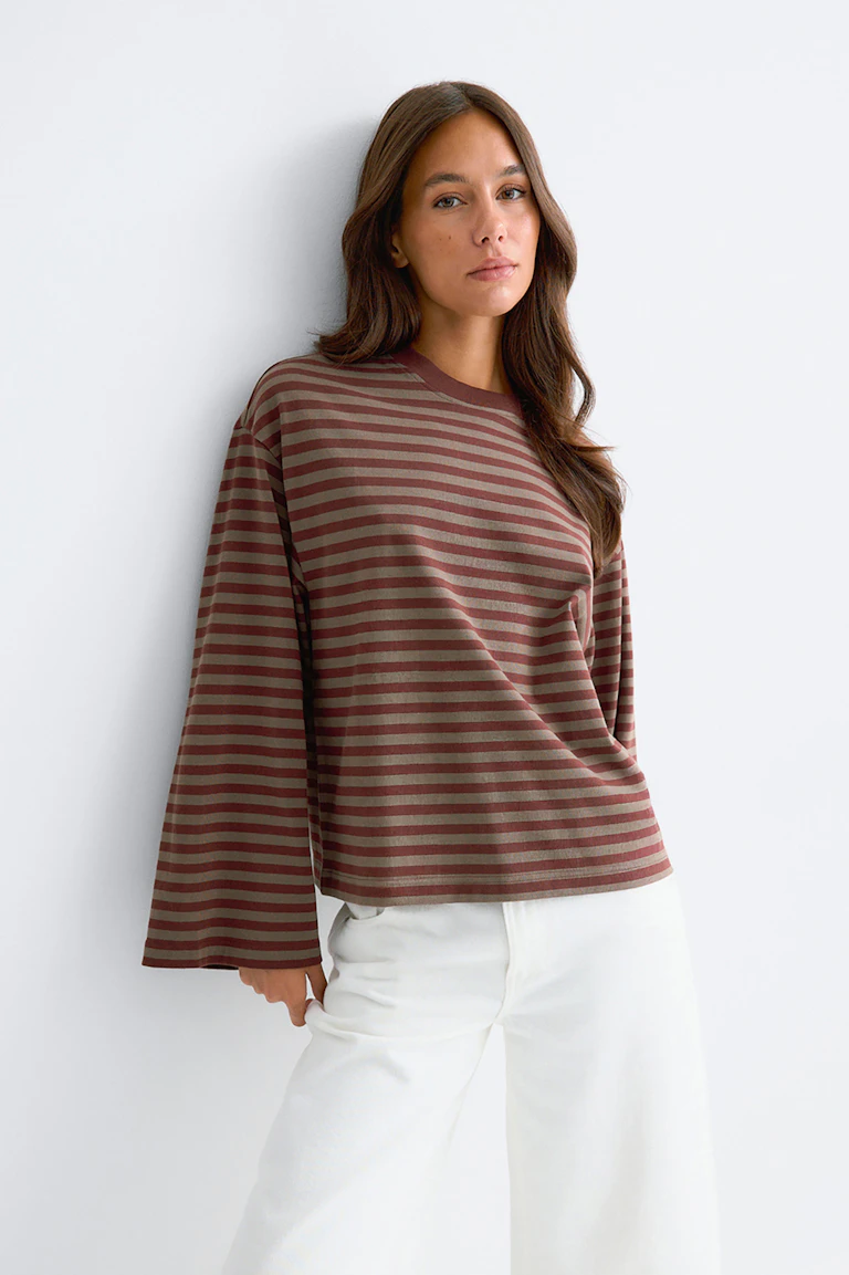 Haut à manches longues rayé marron et taupe, aux manches larges, associé à un pantalon blanc.
