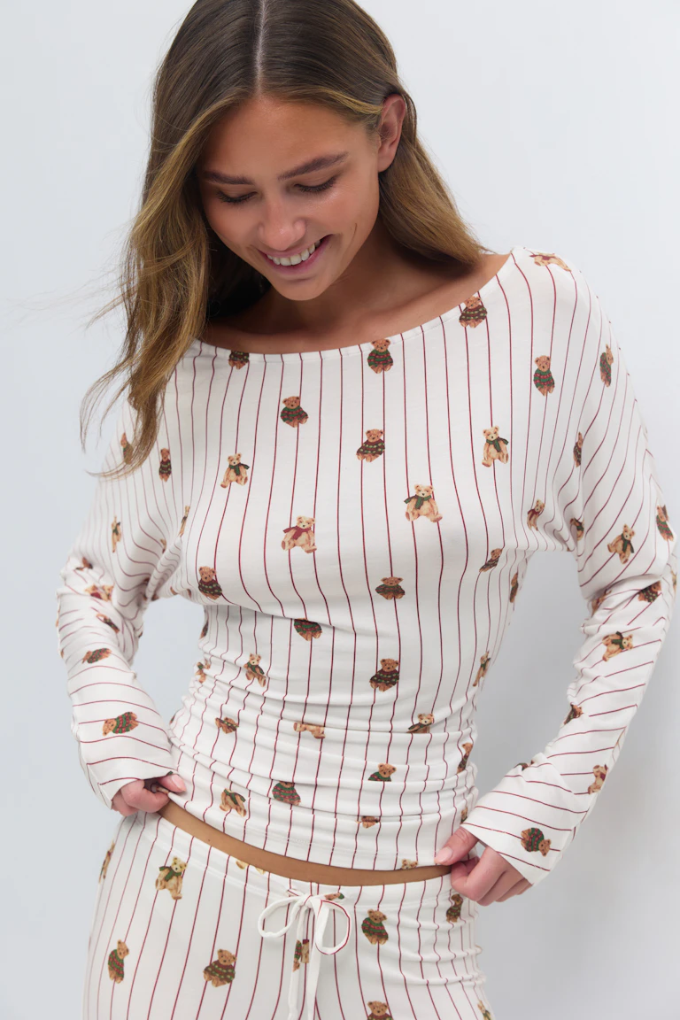 Cremeweißes langärmeliges Oberteil mit Bootsausschnitt und passende Lounge-Hose mit Tunnelzug, dünnen roten Längsstreifen und verstreutem Teddybär-Motiv.