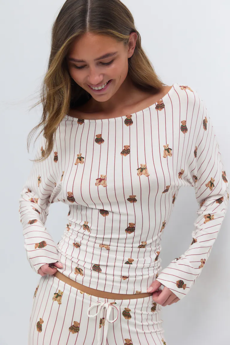 Cremeweißes langärmeliges Oberteil mit Bootsausschnitt und passende Lounge-Hose mit Tunnelzug, dünnen roten Längsstreifen und verstreutem Teddybär-Motiv.