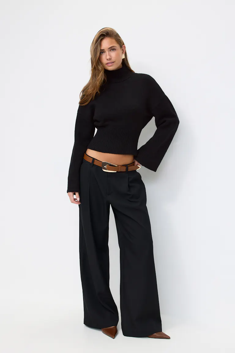 Black cropped ribbed turtleneck sweater with long sleeves, high-waisted wide-leg black trousers, brown leather belt with gold buckle, and brown pointed-toe heels.