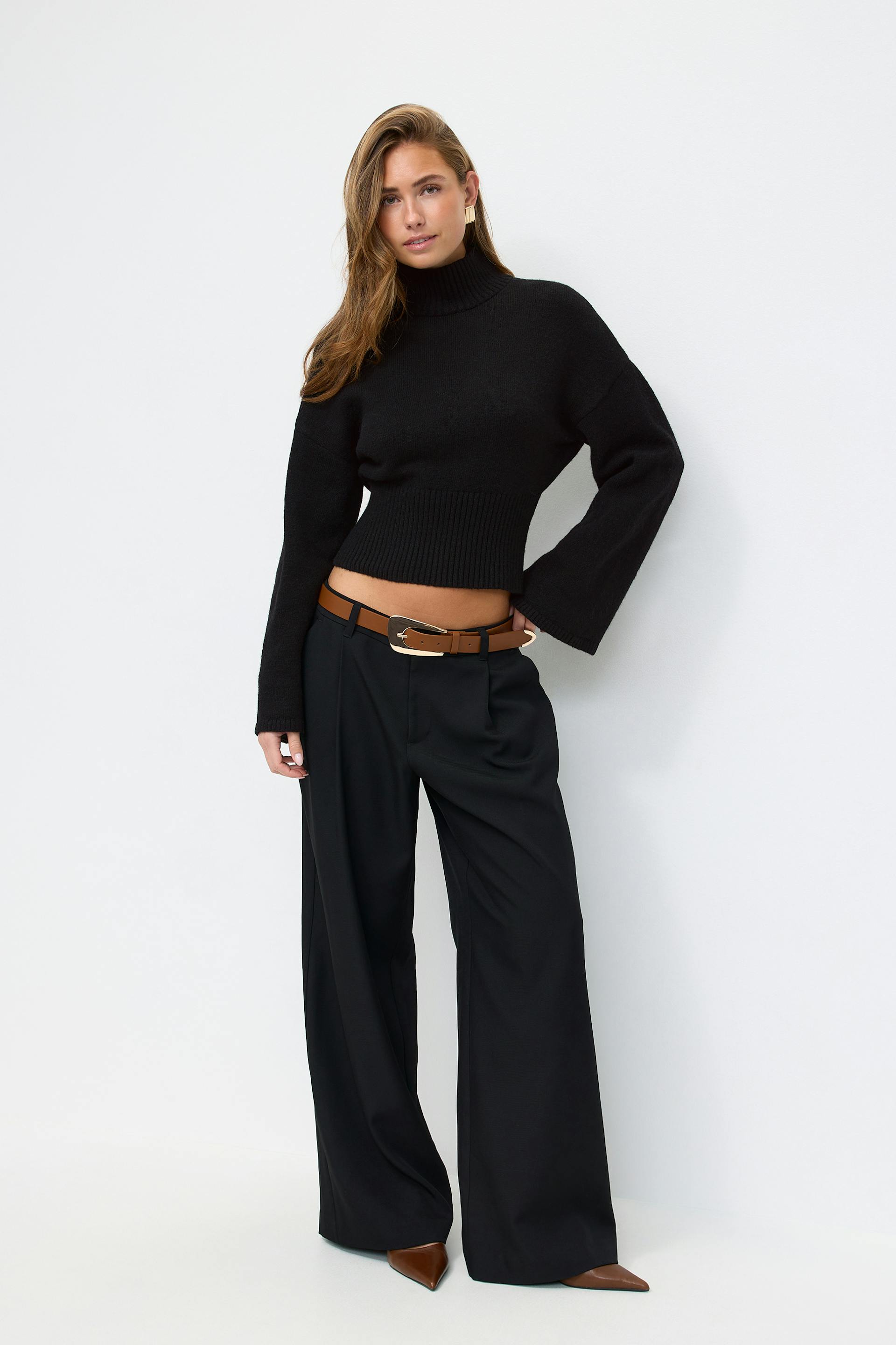 Sort cropped ribbet rullekravesweater med lange ærmer, højtaljede sorte bukser med brede ben, brunt læderbælte med guldspænde og brune spidse hæle.