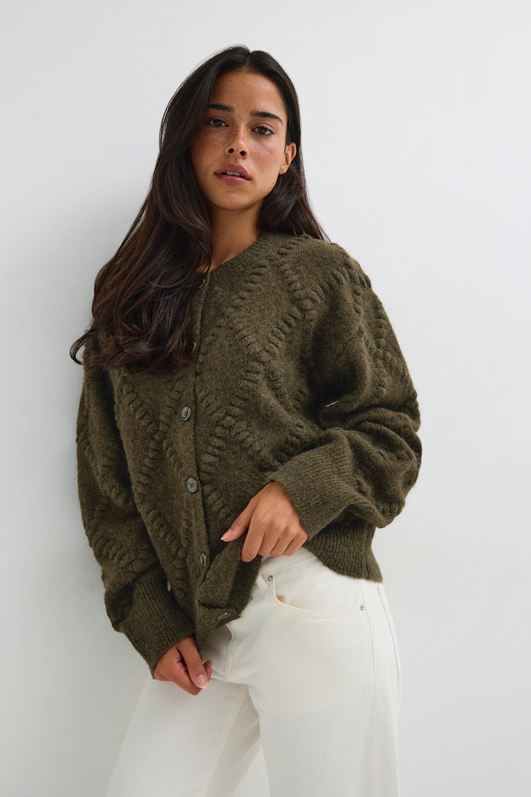Olivgrüne Strickjacke mit Knopfleiste und Strukturmuster, kombiniert mit einer weißen Hose.