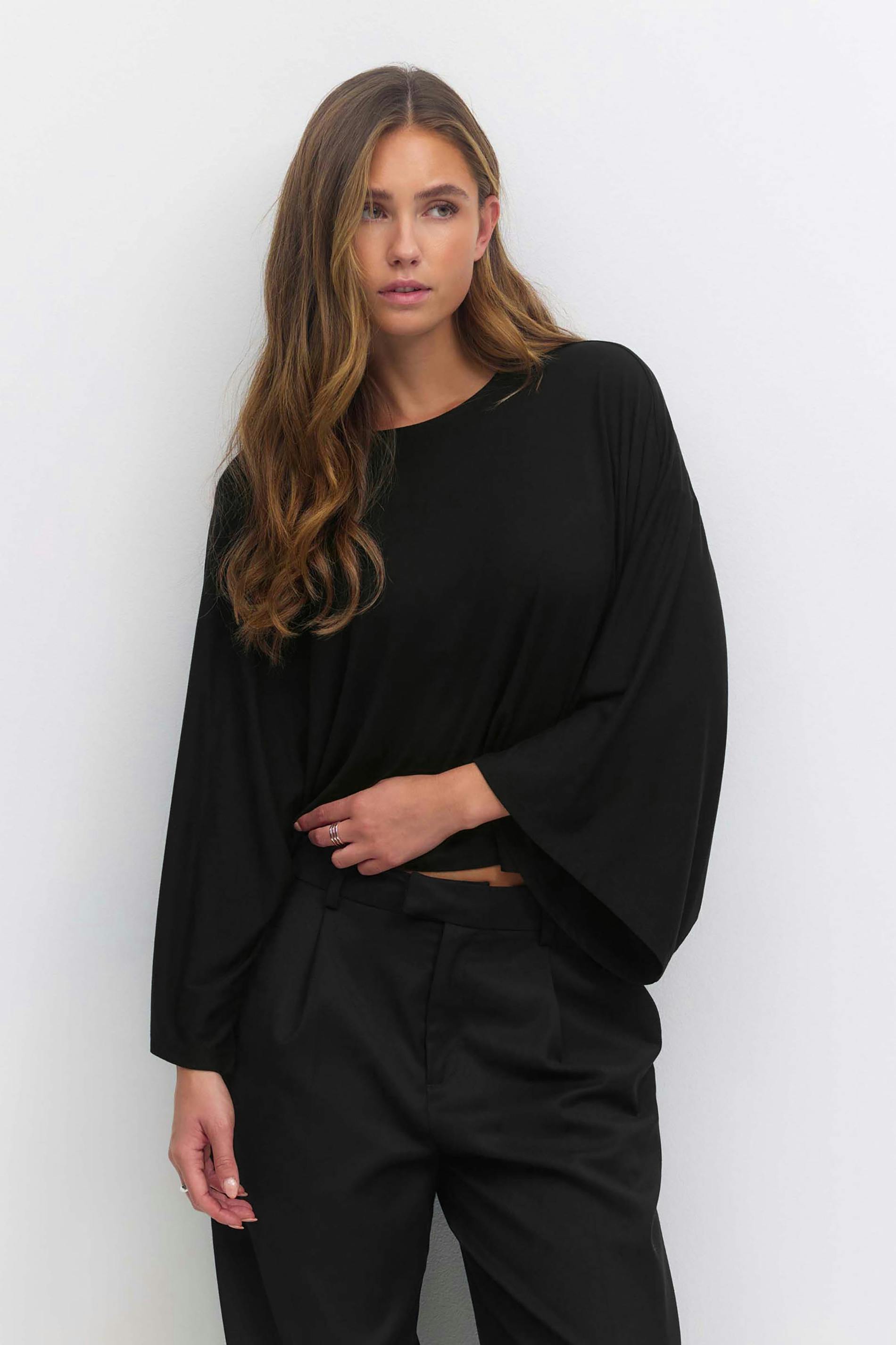 Zwarte oversized top met lange mouwen en wijde mouwen, gecombineerd met een zwarte getailleerde broek.