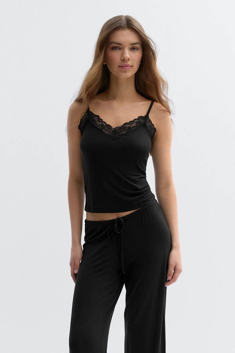 Caraco noir ajusté avec encolure en V en dentelle et fines bretelles spaghetti, associé à un pantalon de détente noir à cordon de serrage.