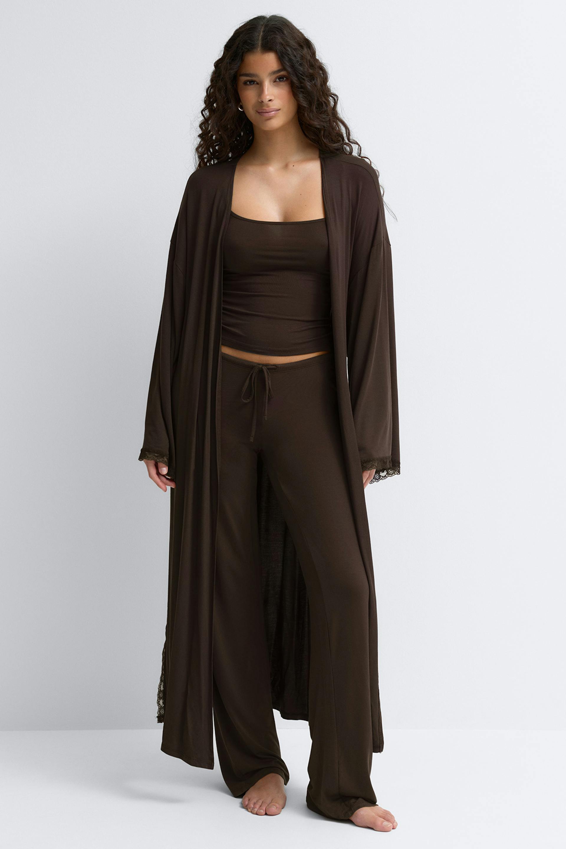 Long chocolate-brown wrap robe with wide kimono sleeves and lace trim at cuffs and hem, tied at the waist over matching loose trousers and a white camisole.