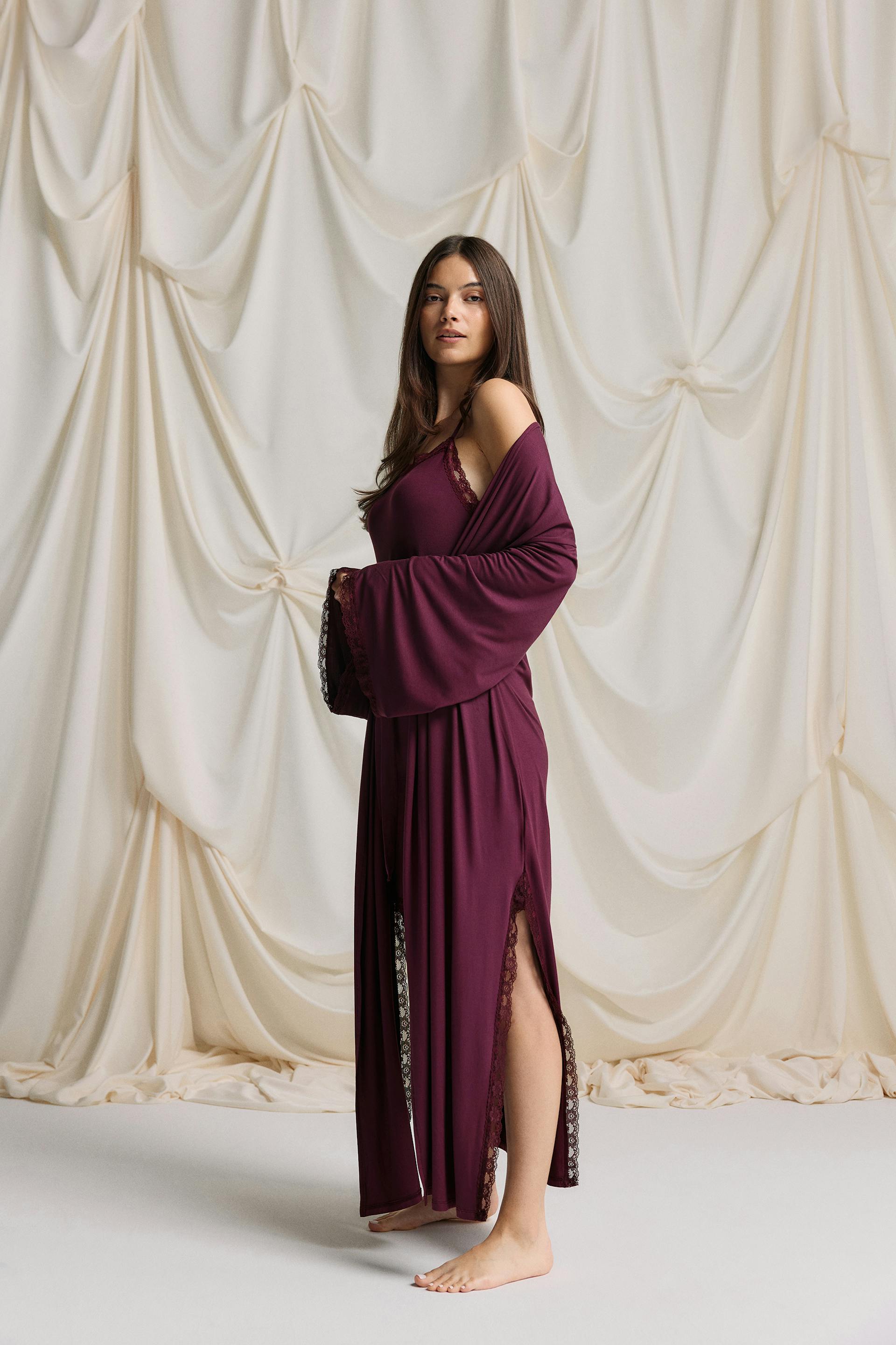 Floor-length burgundy robe layered over a matching lace-trim camisole slip; robe features wide bell sleeves and a high side slit with lace trim.