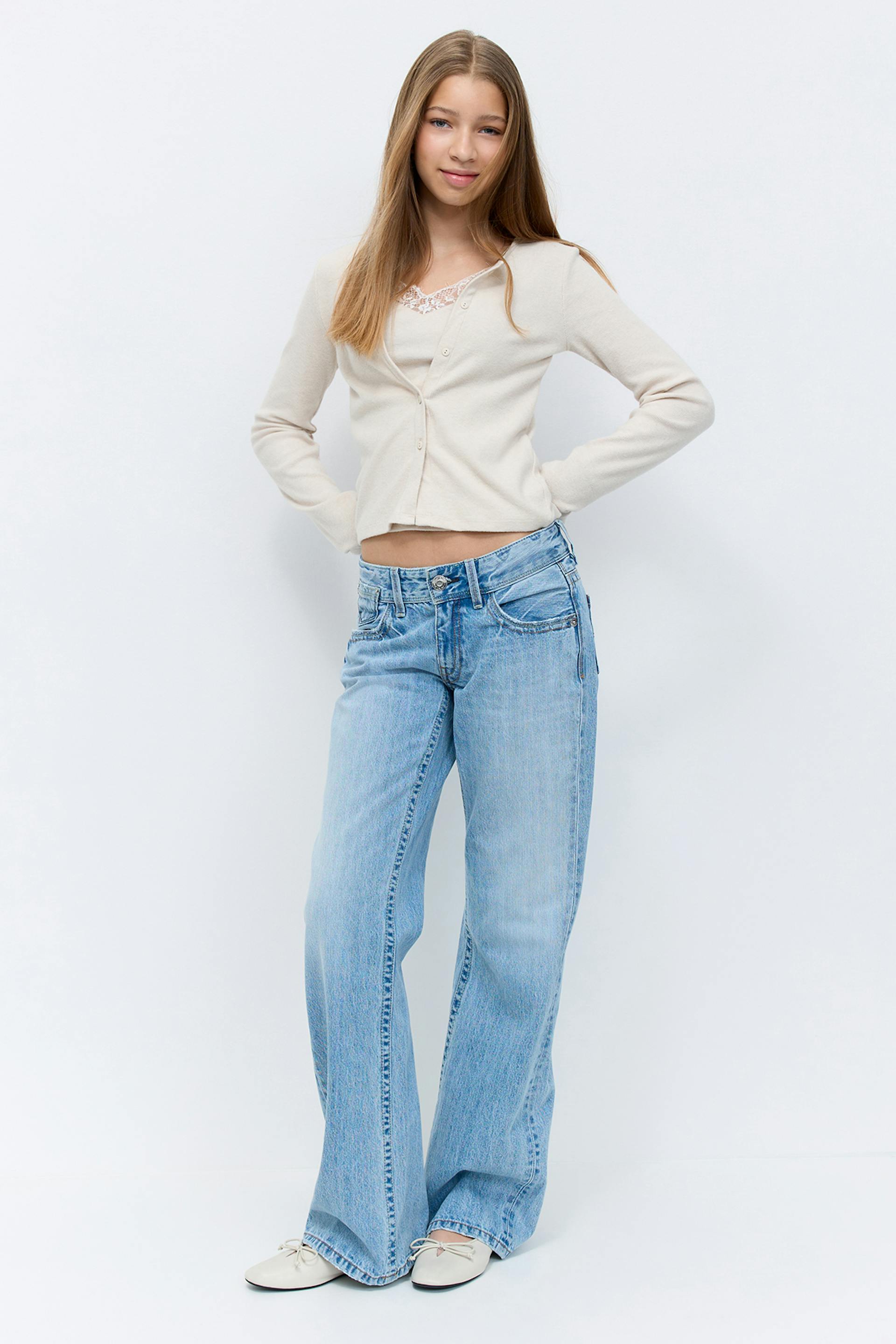 Beige long-sleeve buttoned cropped cardigan over a lace-trimmed camisole, light-wash low-rise wide-leg jeans, and cream ballet flats with bows.
