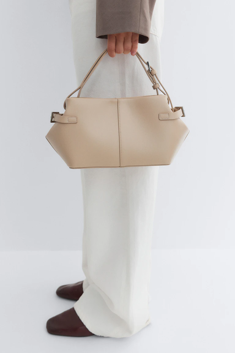 Beige strukturert veske med doble håndtak, stylet med hvite bukser med vide ben, brune spisse sko og en taupefarget langermet blazer.