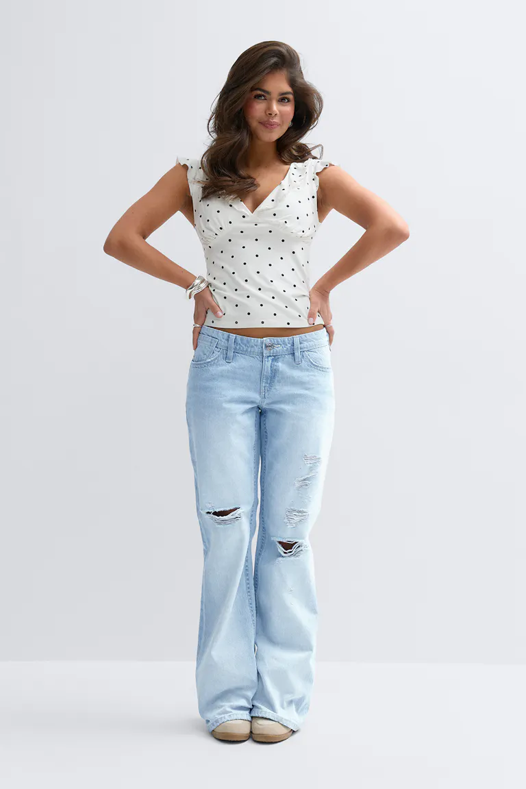 White long-sleeve sweater with lace V-neck inset, light-wash distressed wide-leg jeans with knee and thigh rips, and beige slip-on shoes.