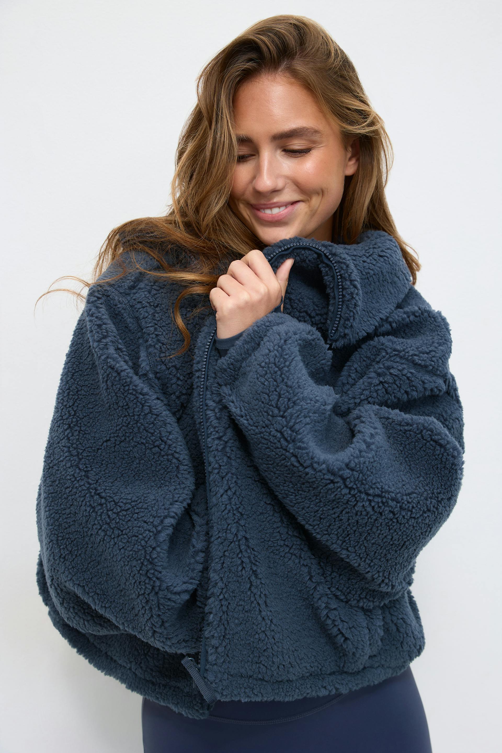 Oversized navy blue sherpa fleece zip-up jacket with high collar, paired with navy leggings.