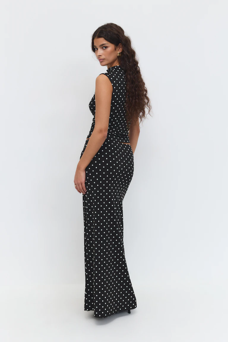 Fitted sleeveless high-neck black crop top paired with a matching high-waisted, floor-length black skirt, both featuring a white polka-dot print.