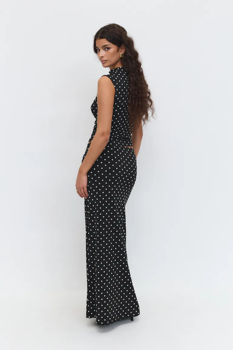 Tailliertes ärmelloses schwarzes Crop-Top mit hohem Halsausschnitt und dazu passender, bodenlanger schwarzer Rock mit hoher Taille, beide mit weißem Tupfenmuster.