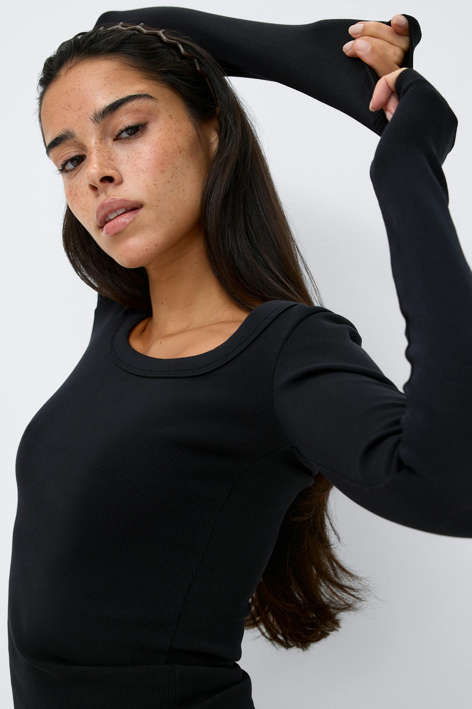 Svart, figursydd, langermet topp i ribbestrikk med utringning og forlengede ermer med tommelhull; tynt, brunt, bølget pannebånd.