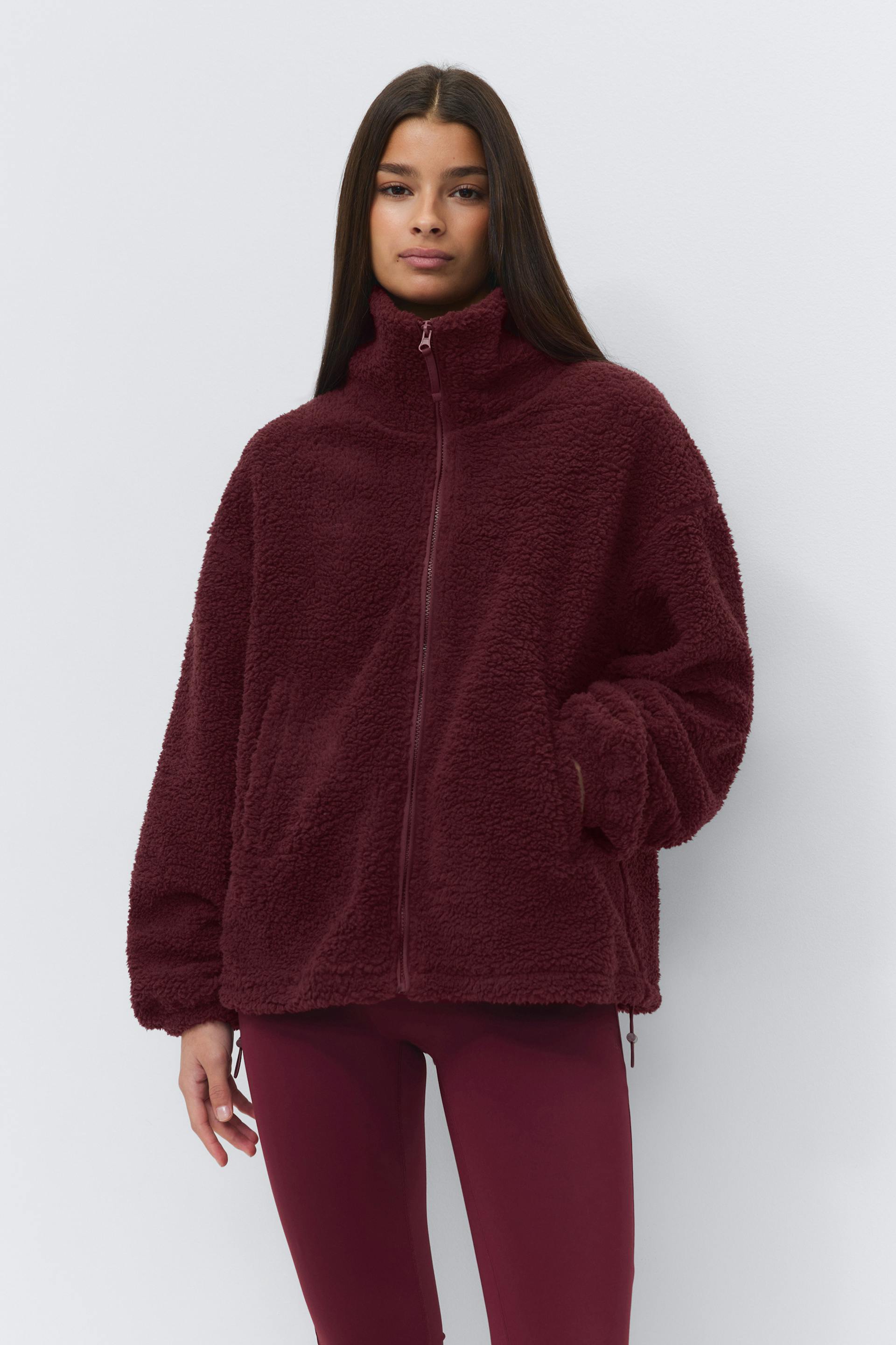 Burgunderfarbene Sherpa-Jacke mit Reißverschluss, hohem Trichterkragen und Seitentaschen, kombiniert mit taillierten burgunderfarbenen Leggings.
