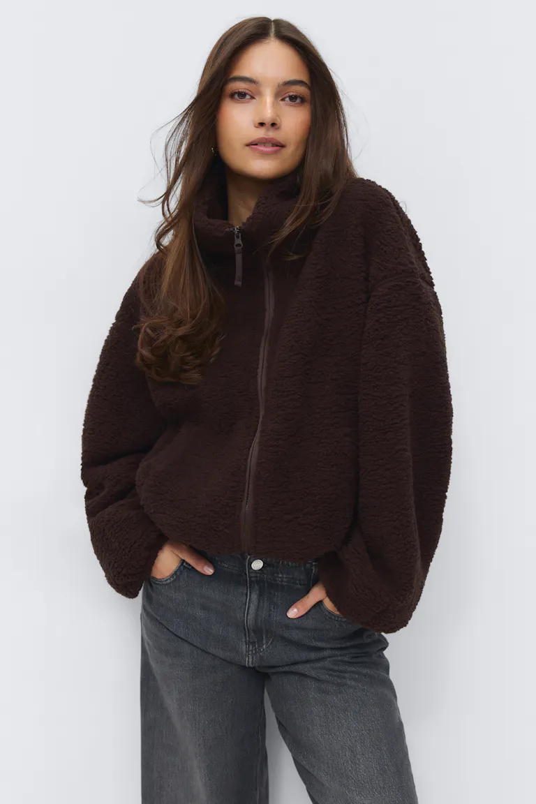 Veste zippée en sherpa marron foncé avec col cheminée et manches volumineuses, associée à un jean taille haute délavé gris noir.