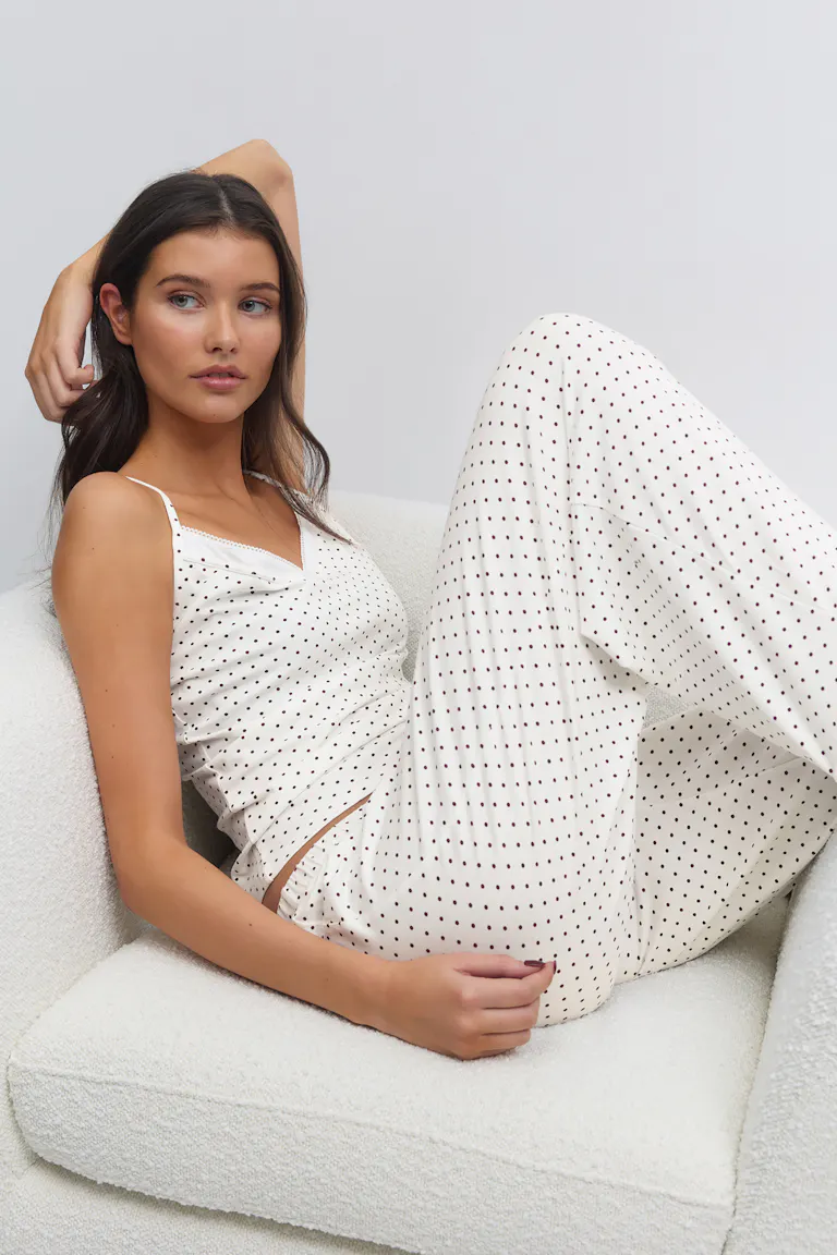 Kermanvalkoinen pilkullinen camisole, jossa on ohuet spagettihihnat, yhdistettynä yhteensopiviin leveälahkeisiin pilkullisiin pyjamahousuihin.