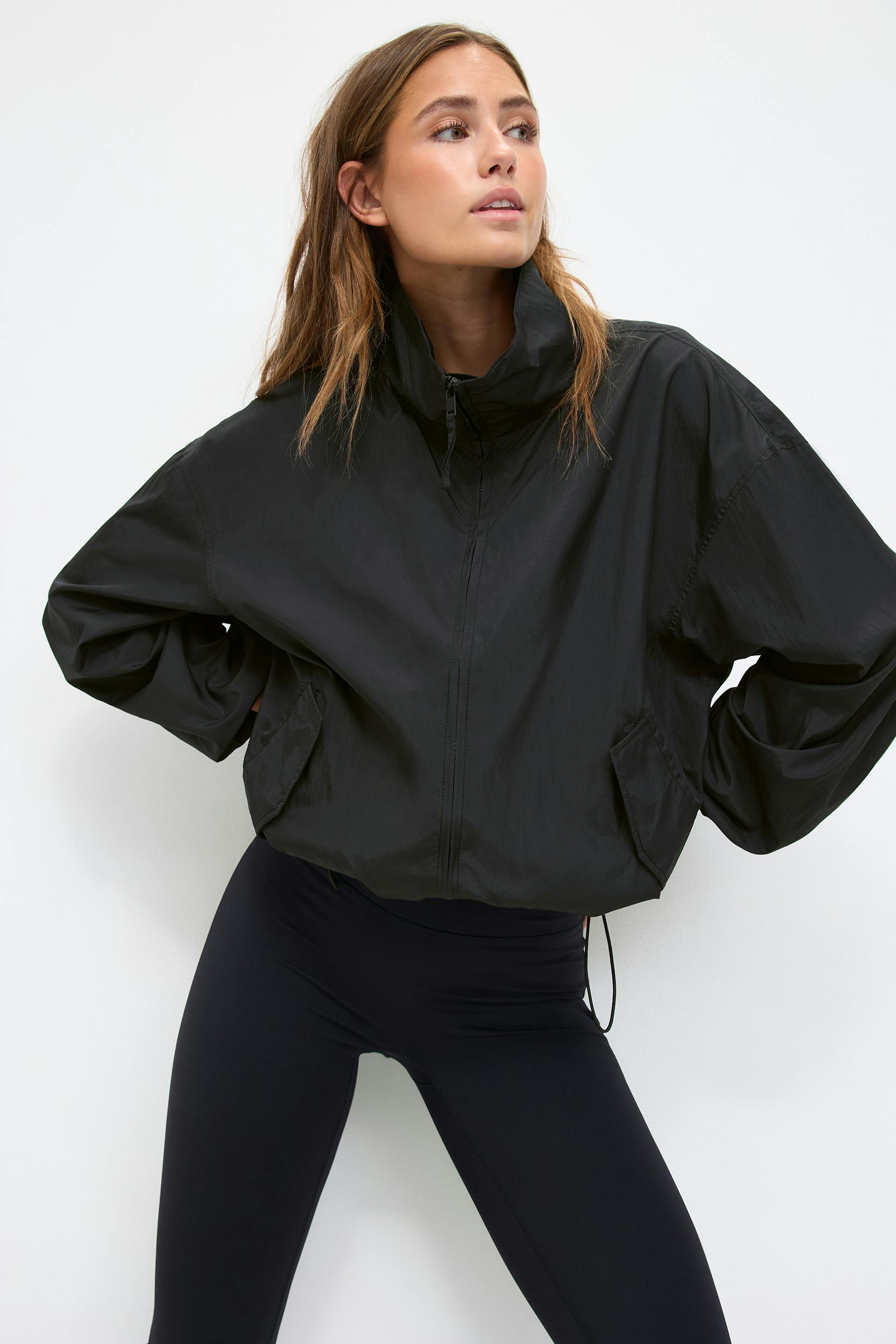 Black high-neck, zip-up cropped windbreaker with oversized long sleeves and front flap pockets, paired with high-waisted black leggings.