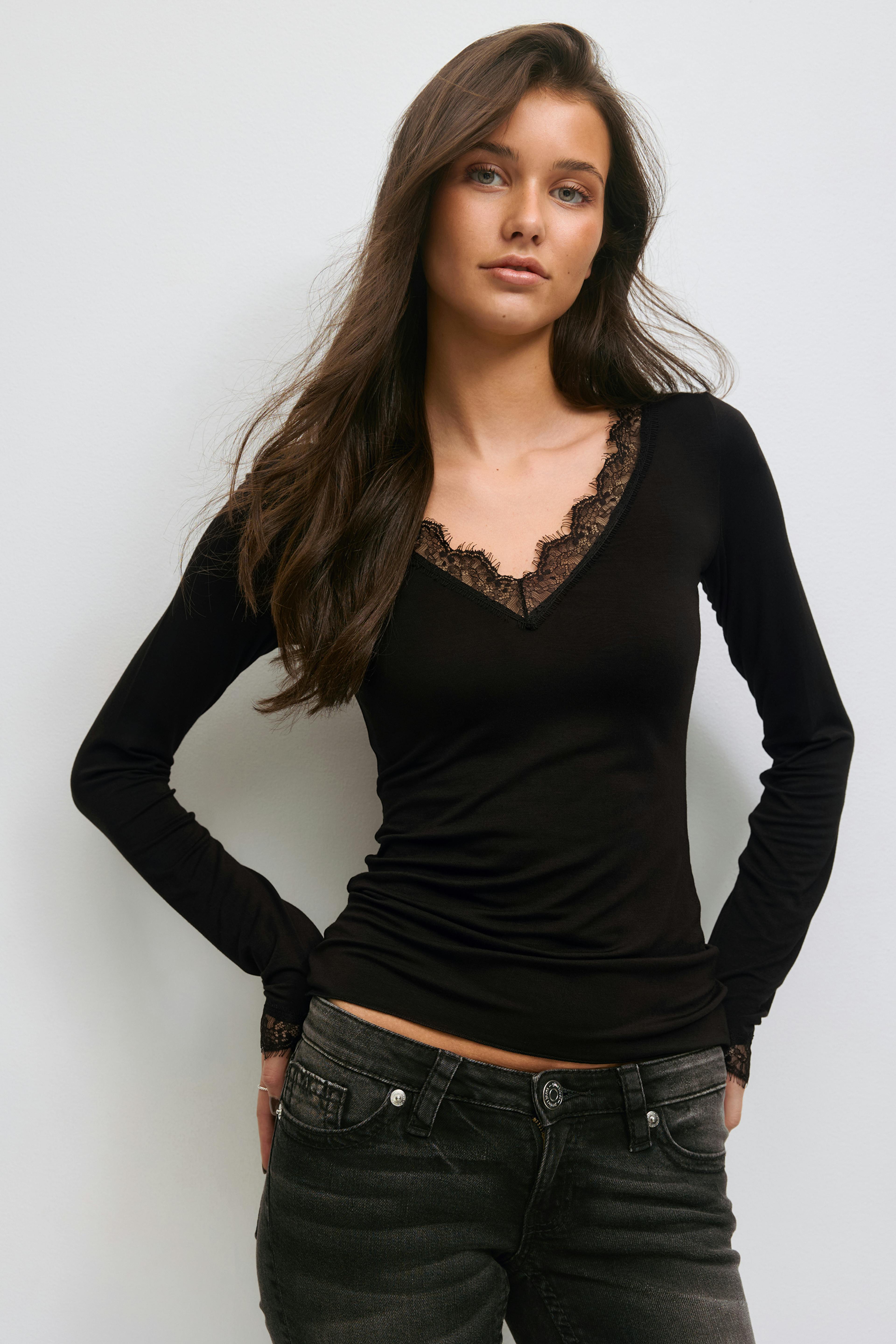 Fitted black long‑sleeve V‑neck top with delicate lace trim at the neckline and cuffs, paired with faded black low‑rise jeans.