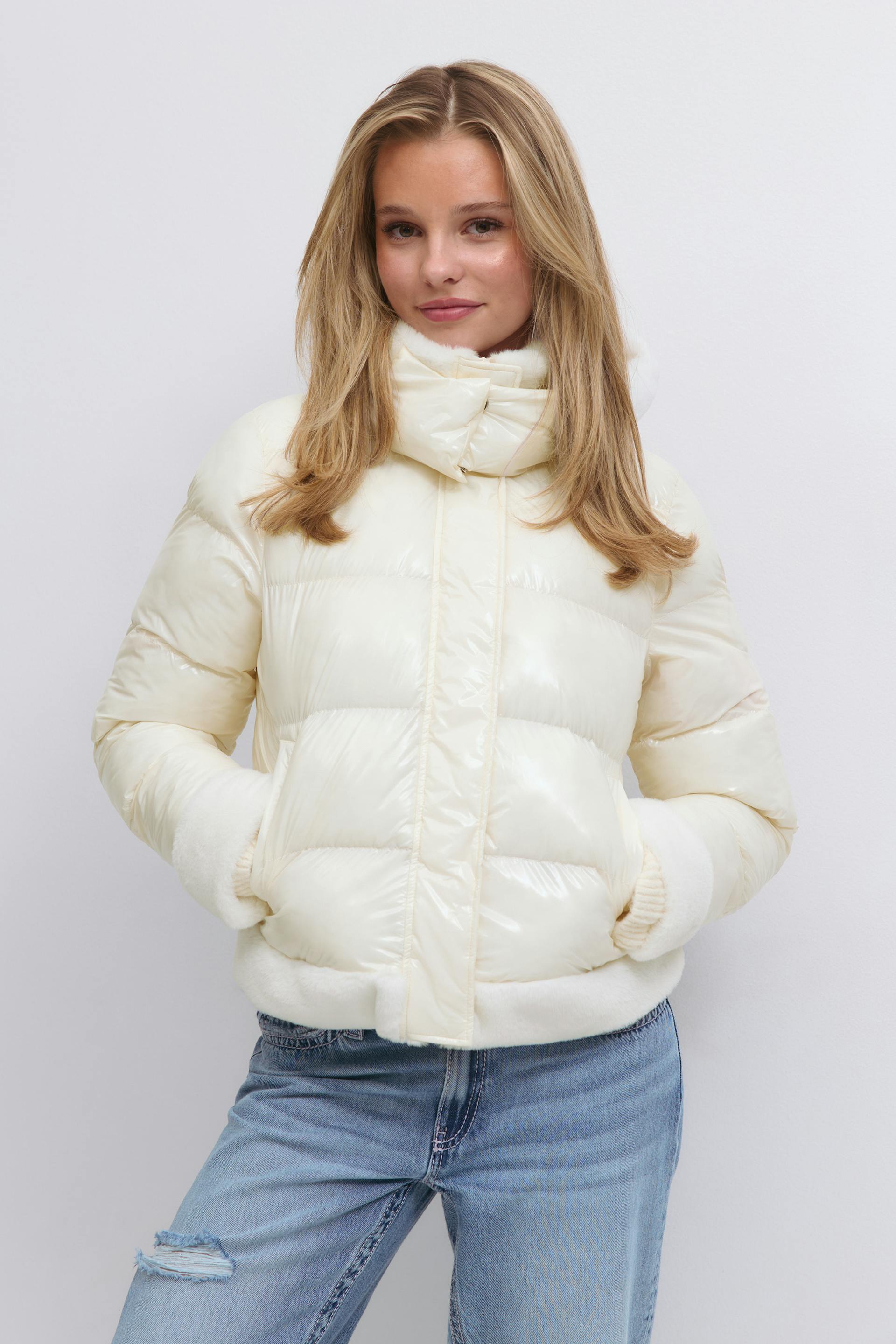 Cremefarvet, blank pufferjakke med høj tragtkrave, vandret quiltning og plysbesætning ved manchetter og forneden, sat sammen med letvaskede, slidte jeans.