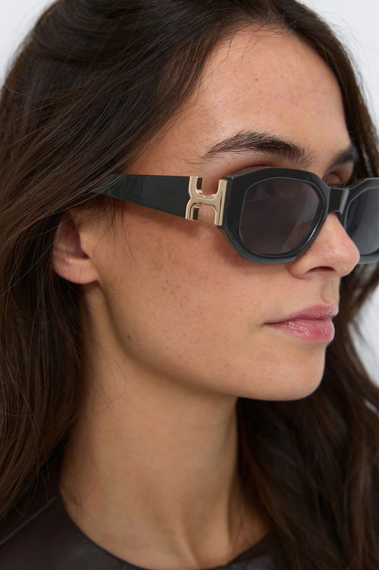 Schwarze Acetat-Sonnenbrille mit dunklen Gläsern und goldfarbenen H-förmigen Bügeln; Oberteil aus dunklem Leder.