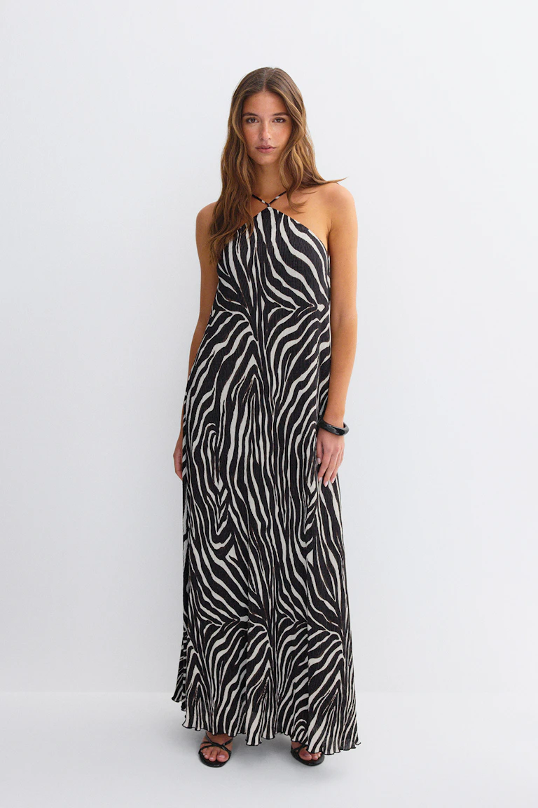 Mouwloze maxi-jurk met halternek in een zwart-witte zebraprint, gestyled met zwarte strappy sandalen en een zwarte manchet-armband.