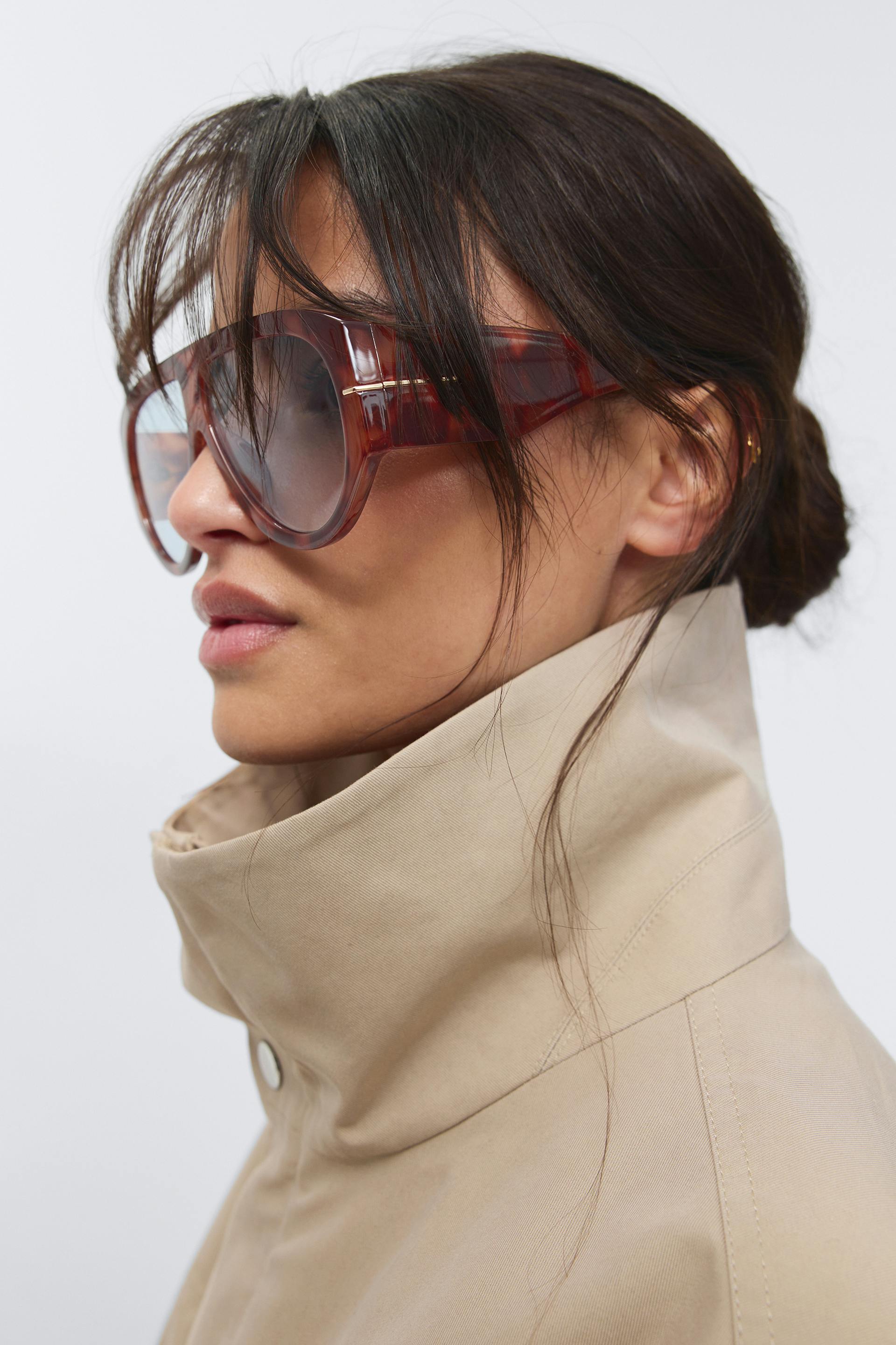Beige high-collar coat paired with oversized brown tortoiseshell sunglasses.