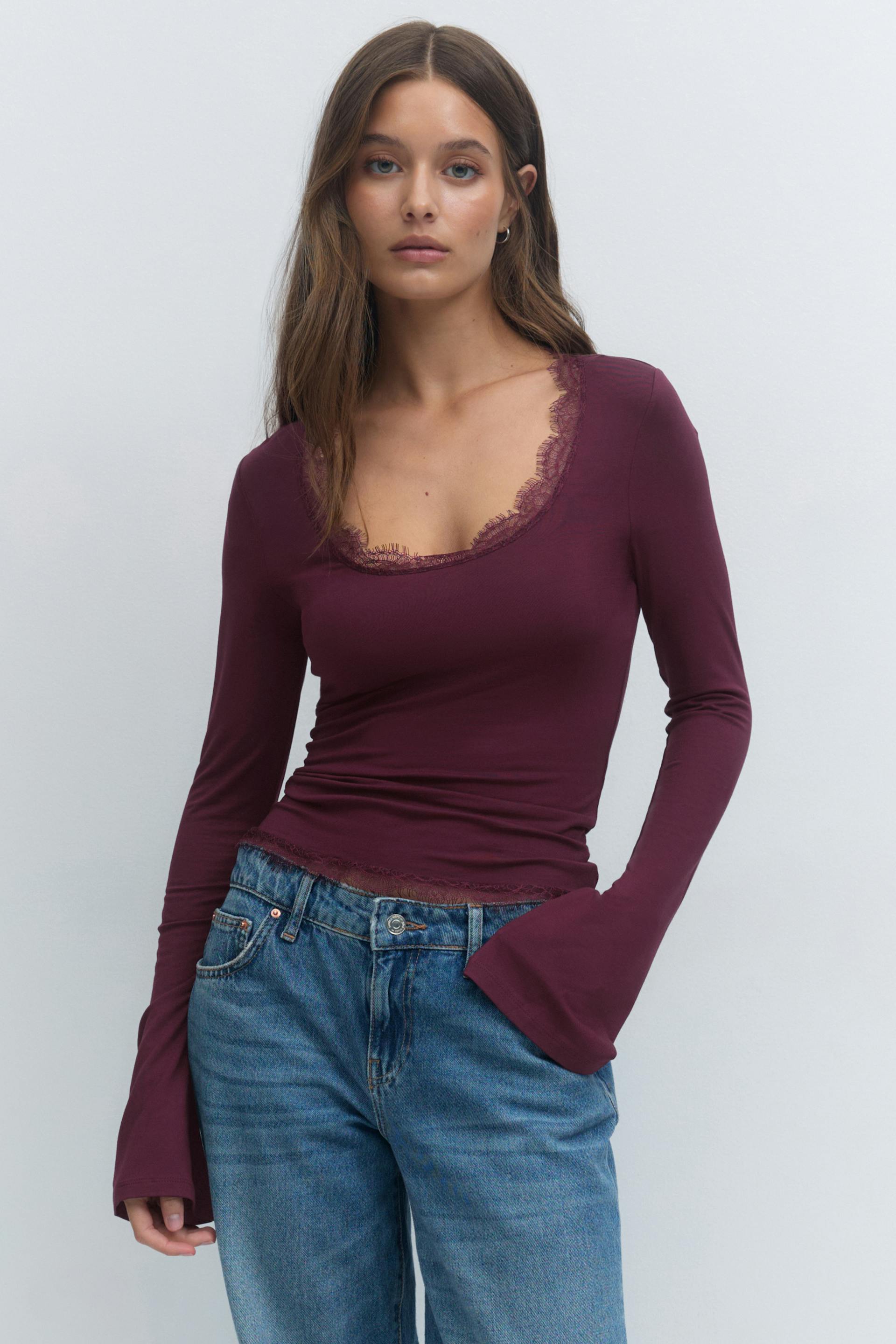 Long-sleeve plum scoop-neck top with delicate lace trim at the neckline and hem, paired with mid-blue high-waist relaxed-fit jeans.