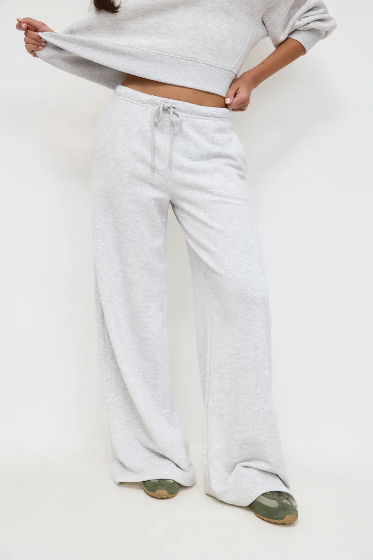 Schwarzes Tank-Top mit Rundhalsausschnitt, hellgraue Jogginghose mit weitem Bein und Kordelzug, dazu ein passendes graues Sweatshirt, das in der Taille gebunden wird, und Ballettschuhe mit Leopardenmuster.