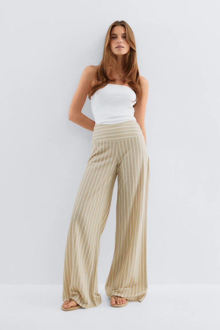 Top ajusté blanc à bretelles associé à un pantalon large beige à taille haute et à rayures verticales blanches, et à des sandales plates beiges.
