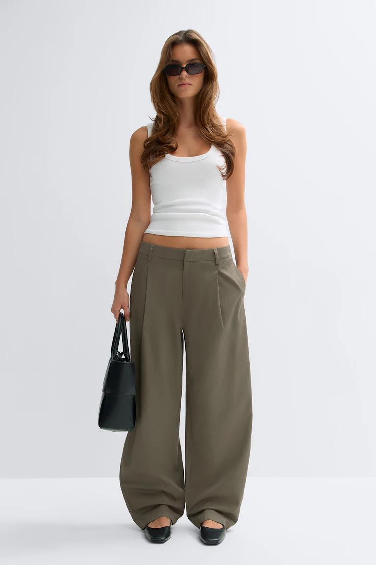 Débardeur blanc sans manches à encolure dégagée associé à un pantalon large kaki à taille haute, des chaussures noires à bout carré, un sac à main noir structuré et des lunettes de soleil rectangulaires foncées.