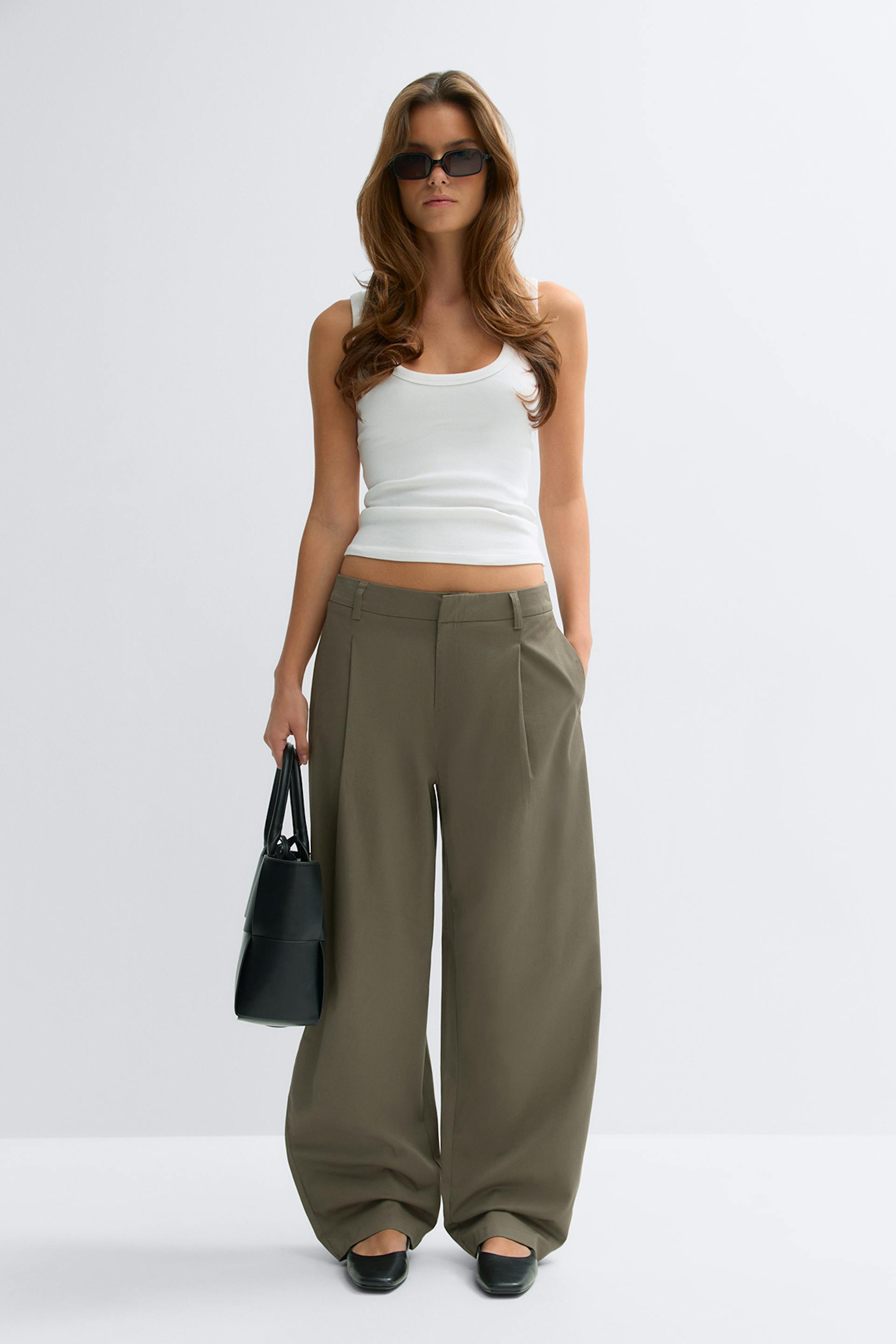 Sleeveless white scoop-neck tank top paired with high-waisted khaki wide-leg trousers, black square-toe flats, a black structured handbag and rectangular dark sunglasses.