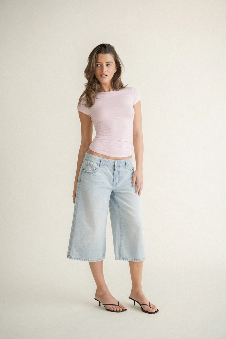 T-shirt ajusté à manches courtes et col ras du cou rose pâle, associé à une jupe-culotte en denim large et délavé et à des sandales thong noires à petits talons.