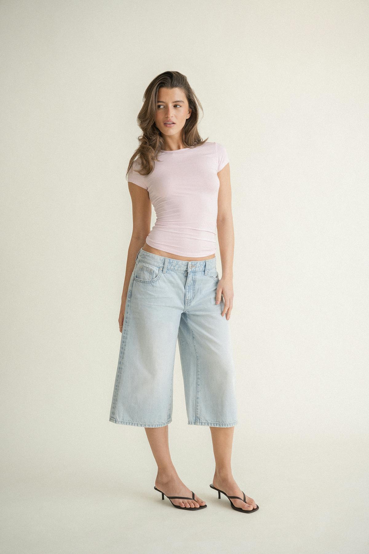 T-shirt ajusté à manches courtes et col ras du cou rose pâle, associé à une jupe-culotte en denim large et délavé et à des sandales thong noires à petits talons.